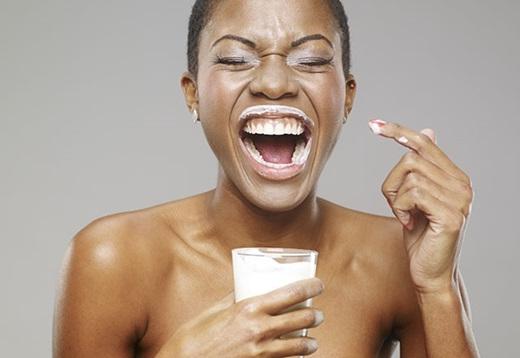 woman holding glass of milk with milk around her lips