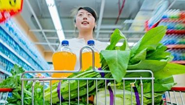 一个年轻人在杂货店购物，购物车里放着蔬菜和果汁