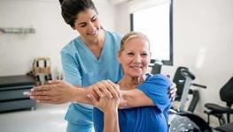 Physical therapist holding senior patient while she stretches her shoulder
