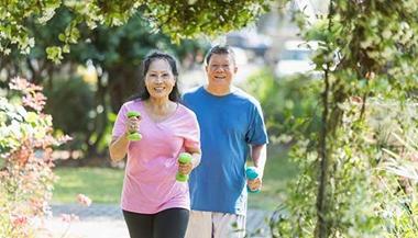 a smiling couple walking with weights outdoors