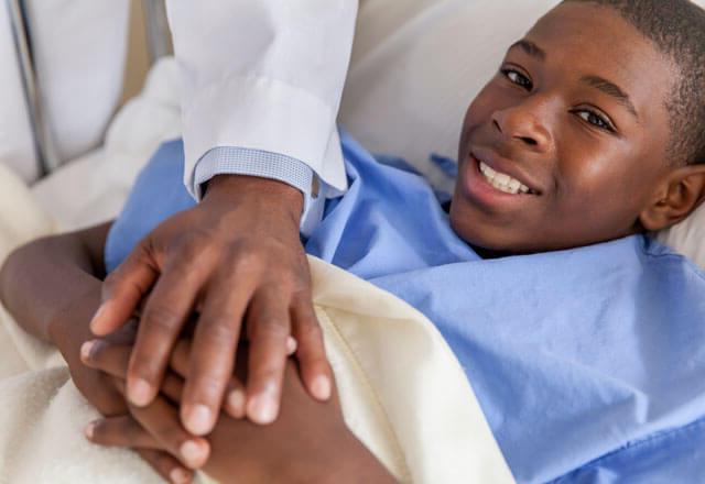 child in a hospital bed with his doctor's hands on top of his