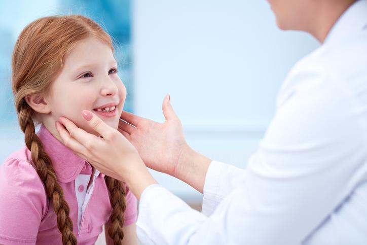 A physician is touching the underside of a girl's chin on either side to check her lymph nodes