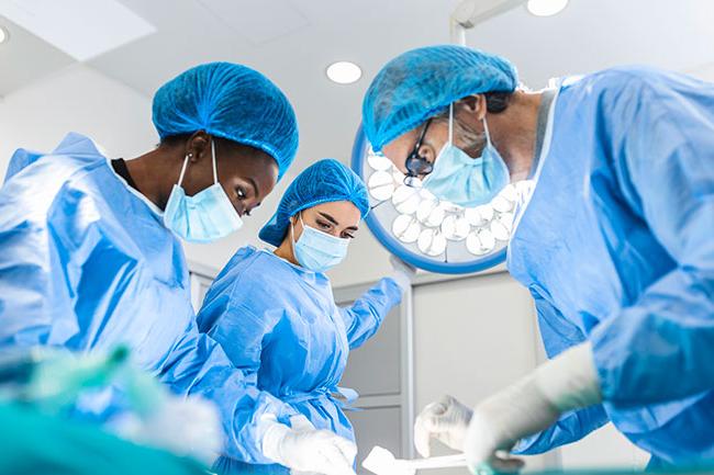 Three doctors in masks and gowns with surgical equipment